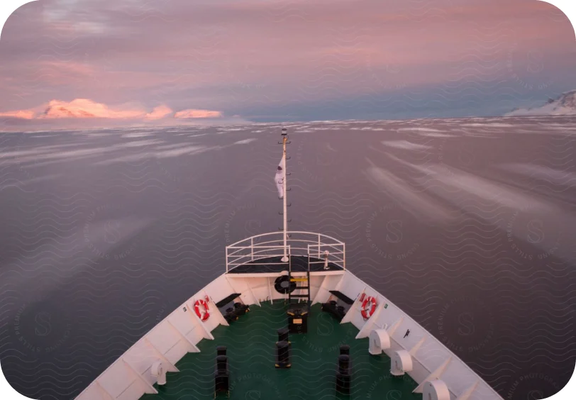 The bow of a cargo ship at sea under a pink dawn sky