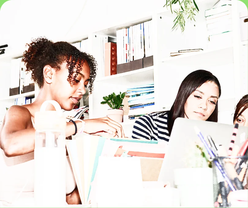 Two colleagues working at a desk in front of a colourful bookshelf — too much contrast