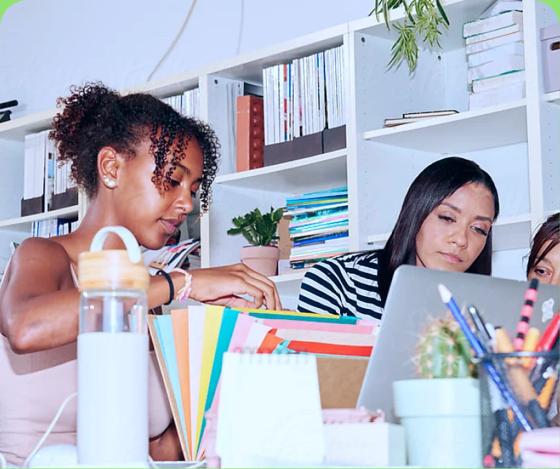Two colleagues working at a desk in front of a colourful bookshelf — too cool
