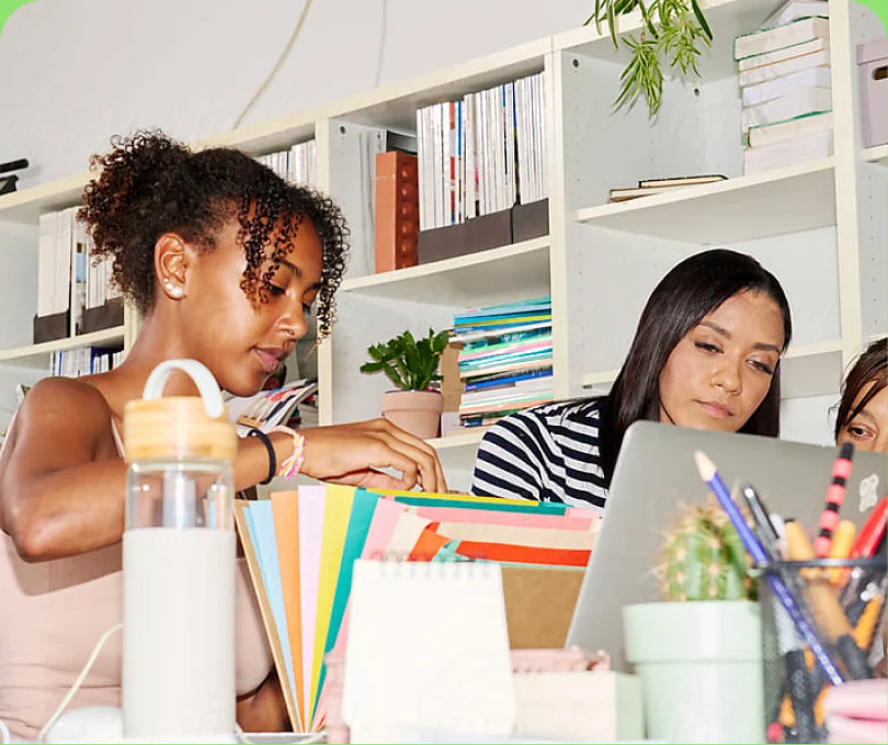 Two colleagues working at a desk in front of a colourful bookshelf — ideal image