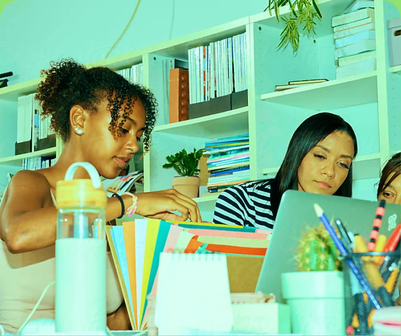 Two colleagues working at a desk in front of a colourful bookshelf — color-washed
