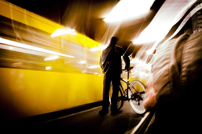 Man standing, holding his bicycle, while the scene whirls around him. 